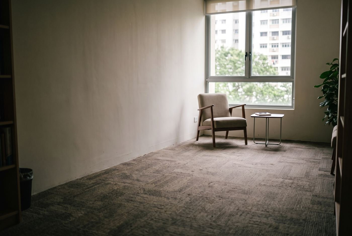 A single armchair and a small side table by a window in an otherwise
empty room, late morning light across the floor.